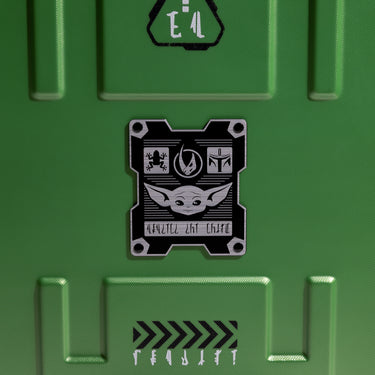 Black enamel badge on the back of a star wars grogu themed luggage with a photo of grogu, a mudhorn symbol and a Mandalorian symbol on a green background