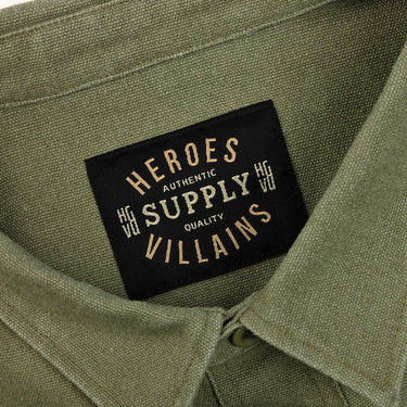 The photo shows a close up of a green shirt jackets label. The label says "Heroes Villains, Authentic Supply Quality"