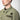 The photo shows a close up of a man facing the left. The photo is showing a close up detail of a green shirt jacket. The Photo is featuring two patches above a shirt pocket. The top patch is circular and features a skull and cross bones logo. The bottom patch has the text "H.V. MFG."