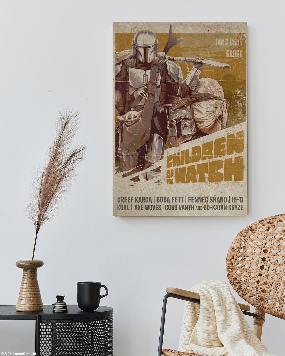 Poster of Mando holding the child on a wall in a room with a black side table and wicker chair.