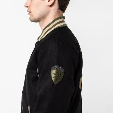 The photo shows a man facing left to show off a patch on the right sleeve of a jacket. The patch says "cadet "with a crossbones logo below