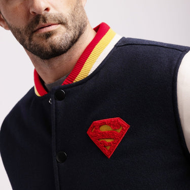 Man wearing a Navy varsity jacket with a Superman logo on a white background