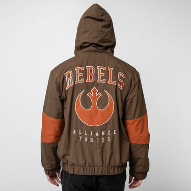 A person standing backwards to show the back of a Star Wars-themed hooded windbreaker jacket. The jacket is primarily brown with orange accents. The design features large, bold text reading 'REBELS' across the upper back, with the Rebel Alliance emblem in orange below it. Beneath the emblem, the words 'ALLIANCE FORCES' are printed in a smaller font. The jacket has an elastic waistband and cuffs, with a color-blocked pattern matching the front design.
