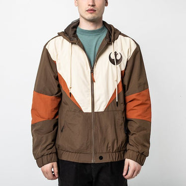 A man in a Star Wars-themed hooded windbreaker jacket featuring a Rebel Alliance emblem on the left chest. The jacket has a color-blocked design in brown, beige, and orange, with a front zipper, adjustable drawstrings on the hood, elastic cuffs, and two zippered pockets. The overall aesthetic is inspired by the Rebel pilot uniforms from the Star Wars universe