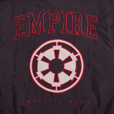 The back of a Star Wars-themed hooded windbreaker jacket, primarily black with red and white accents. The design features large, bold text reading 'Empire' across the upper back, with the Imperial Army emblem in white with a red boarder it. Beneath the emblem, the words 'Imperial Army' are printed in a smaller font. The jacket has an elastic waistband and cuffs, with a color-blocked pattern matching the front design.