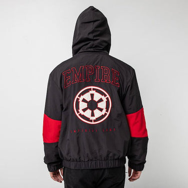 A person standing backwards to show the back of a Star Wars-themed hooded windbreaker jacket, primarily black with red and white accents. The design features large, bold text reading 'Empire' across the upper back, with the Imperial Army emblem in white with a red boarder it. Beneath the emblem, the words 'Imperial Army' are printed in a smaller font. The jacket has an elastic waistband and cuffs, with a color-blocked pattern matching the front design.