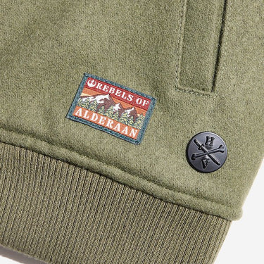 The close up shows a rectangular patch with the words "Rebels of" at the top and "Alderaan" at the bottom. Between the words is a small picture of a forest and mountains.  To the left of the patch is a small circular metal icon featuring the "Heroes and Villains" logo