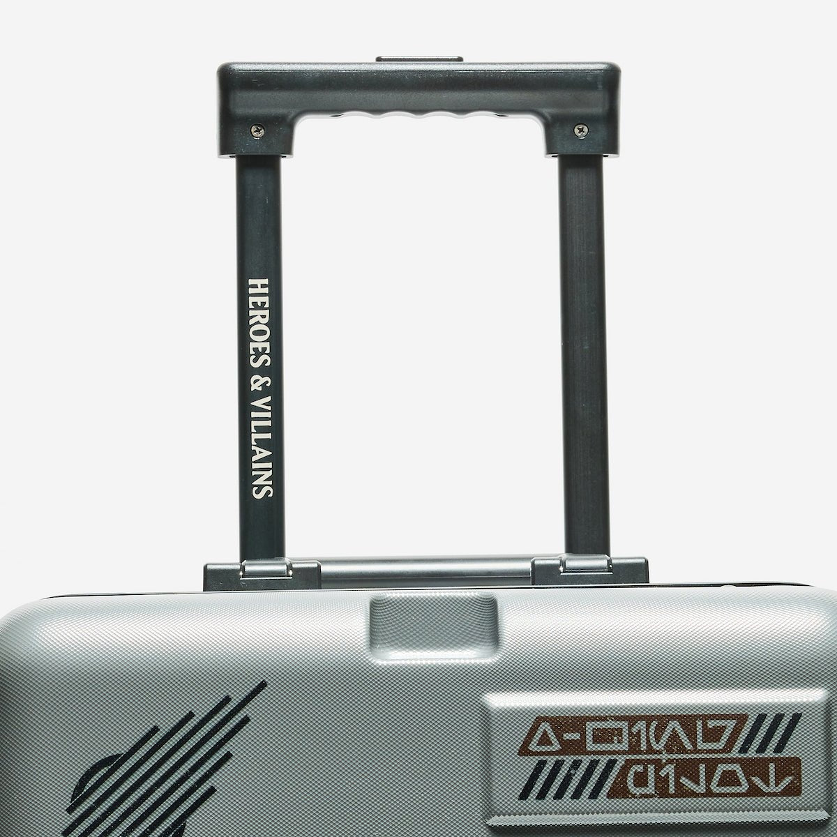 Silver suitcase with 'Heroes & Villains' branding on a white background