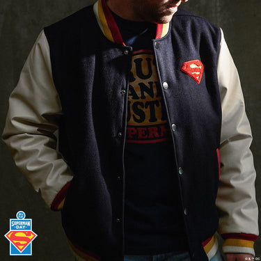 Person wearing a Superman-themed letterman jacket with a logo on a dark background