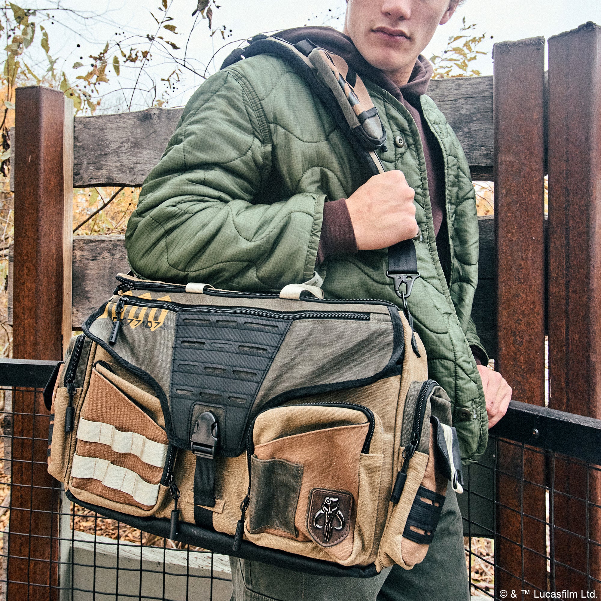 Male carrying the Heroes & Villains Mandalorian Canvas Bike Messenger Bag in olive green and tan, featuring the Mythosaur skull symbol, utility pockets, and an adjustable strap for functionality and style.