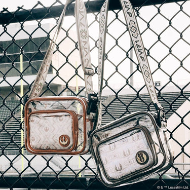 Two clear Star Wars Crossbody bags with printed designs hanging on a chain-link fence.