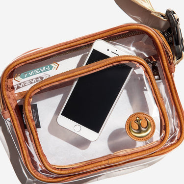 Clear travel pouch with brown trim containing a smartphone and a small item, on a white background.