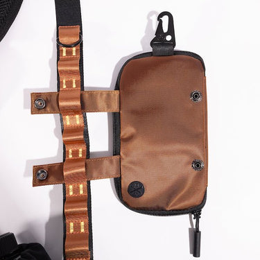 The photo shows a close up detailing of the shoulder strap. Featured is the Blue decorative detailing. The detailing has loops for attaching clips and a tech case. The tech case is pictured to the right side displaying the straps going through the loops. The top loop has a "D"-Ring attached.