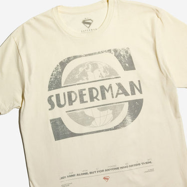 Cream-colored T-shirt featuring a distressed Superman logo and text, with additional small text and symbols printed near the bottom hem.