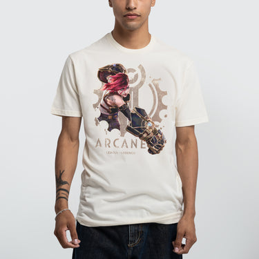 A Male model wearing a cream-colored Arcane x League of Legends t-shirt featuring Vi in an action pose. She has her signature pink hair and wields her massive Hextech gauntlets, detailed with metallic and glowing blue accents. Behind her, a faded Piltover gear emblem adds depth to the design. 'Arcane' and 'League of Legends' are printed below in a bold, distressed font
