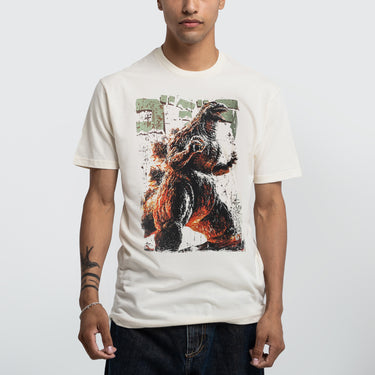 Male modeling Natural-colored T-shirt featuring a vintage-style graphic of Godzilla roaring with a distressed design, Japanese text, and green block lettering.