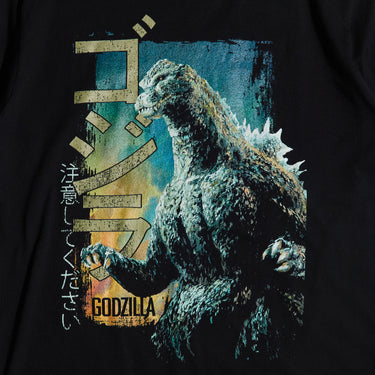 Close-up of a black colored T-shirt featuring a vintage-style graphic of Godzilla roaring with a distressed design, Japanese text, and green block lettering.