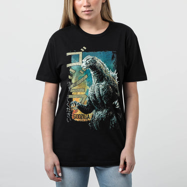 Female modeling Black colored T-shirt featuring a vintage-style graphic of Godzilla roaring with a distressed design, Japanese text, and green block lettering.