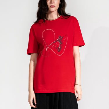 A female model wearing a Dynamic graphic tee featuring a striking silhouette of Daredevil in mid-air, outlined by his signature billy club linework. The bold red background enhances the action-packed design, capturing the essence of Hell’s Kitchen’s guardian.