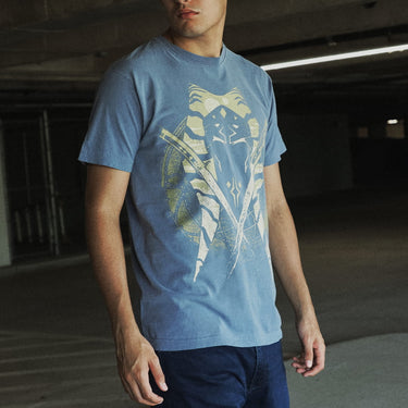 A man wearing a  blue crewneck t-shirt featuring a distressed graphic of Ahsoka Tano's face, crossed lightsabers, and a circular emblem on the front, set against a plain light gray background.