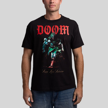 A man wearing a black graphic t-shirt featuring the red 'DOOM' logo and a green armored character print, paired with blue jeans, against a solid gray background.