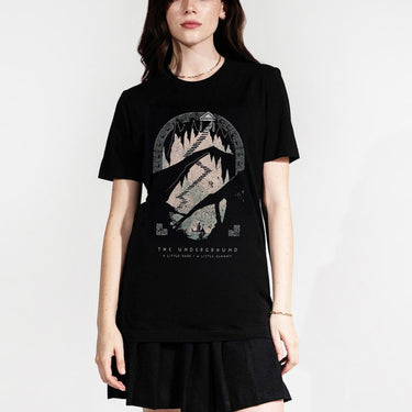 Woman in a Tee with a stylized design of a staircase leading to a temple, with intricate patterns and a boat below