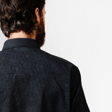 A close up of a man in a button up black shirt with red details in a star wars imperial geometric pattern 