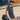 Man wearing a navy blue x-men t-shirt with a yellow logo and cap, carrying a  duffel bag against a brick wall.