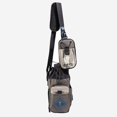 The photo shows a crossbody bag designed for carrying a water bottle. The bag features a drawstring closure at the top, a front zippered pocket, and a blue rubber patch with a geometric design meant for attaching a clip. The adjustable black strap has a padded section for comfort and a blue cord with holes to attach clips and a tech organizer bag. The bag is in a subtle brown with pops of blue and black.